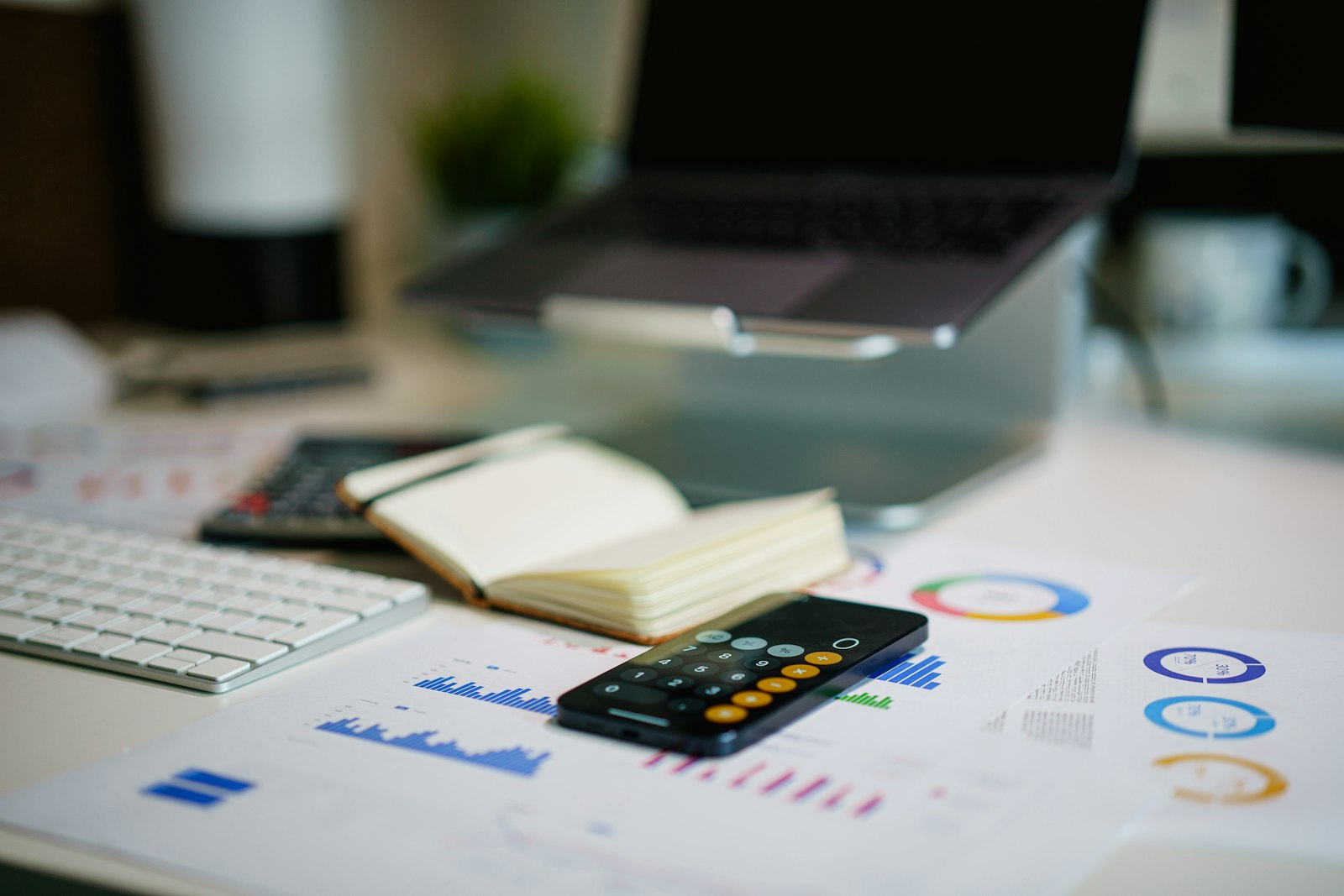 A desk with printed charts, a notebook, and a laptop — reviewing the numbers